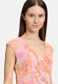 Robe portefeuille à motif floral avec de courtes manches, présentant des teintes de rose et d'orange dans un tissu léger et texturé.