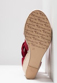 Sandale rouge à talon en forme de coin avec une semelle en corde tissée. La semelle présente le nom de la marque "Tamaris" embossé ainsi que la taille "37". Dessus en tissu lisse avec un design ouvert.