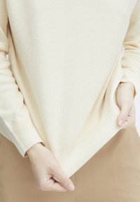 Pull en maille de couleur crème avec des poignets et un ourlet côtelés, présentant une coupe légèrement surdimensionnée et une texture respirante. Design uni.