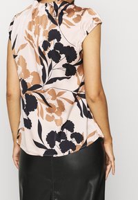 Blumenstoffoberteil in Pink mit schwarzen und braunen Blumenmustern, runder Ausschnitt, kurze Ärmel und seitliche Schlitze am Saum.
