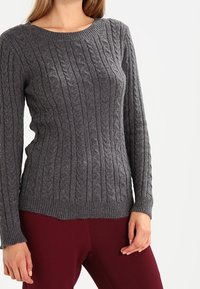 Grå kabelstickad tröja med rund halsringning, långa ärmar och ribbat avslut, tillverkad av en strukturerad ullblandning, i kombination med vinröda leggings.