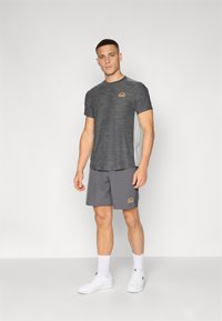 Grå treningst-skjorte med teksturert stoff og logo, sammen med grå shorts. Hvit sneakers og sokker fullfører antrekket. Enkelt, funksjonelt design.