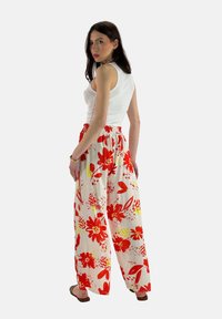 Witte crop top, vloeiende broek met een levendig rood en geel bloemenpatroon, elastische tailleband, lichtgewicht stof, wijd-benige ontwerp.