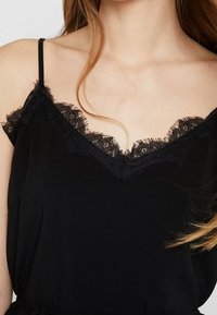 Schwarzes Top mit V-Ausschnitt, verziert mit zarter schwarzer Spitzenborte und dünnen Schulterträgern, aus einem weichen, glatten Stoff gefertigt.
