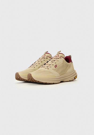 Baskets en mesh et daim beige avec semelles en caoutchouc marron, accents rouges et design à lacets. Comprend un col rembourré et un détail de logo.