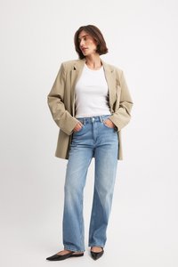 Beige blazerin päällä valkoinen t-paita, yhdistettynä vaaleansinisiin korkeavyötäröisiin farkkuihin. Mustat tasapohjaiset kengät täydentävät asukokonaisuuden. Yksinkertainen muotoilu, rento tyyli.