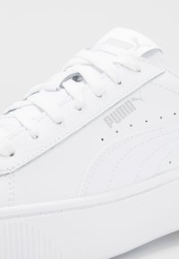 Baskets blanches en cuir lisse avec une semelle texturée. Comprennent des lacets blancs, un logo argenté et des détails perforés.