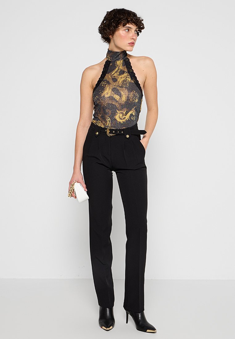 Pantalons taille haute noirs associés à un haut sans manches ajusté à motifs avec des tourbillons dorés et noirs. Les accessoires comprennent une pochette blanche.