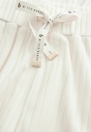 Valkoiset ribattut kangaspajamahousut, joissa on tekstuuripinta. Varustettu vastaavasta kankaasta valmistetulla nauhalla, jossa on kultaiset logot. Vahvistettu elastinen vyötärö.