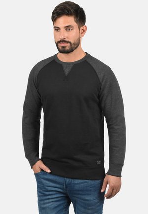 Sudadera negra y gris oscuro con mangas raglán, puños y dobladillo acanalados; fabricada en un tejido suave con una textura lisa.