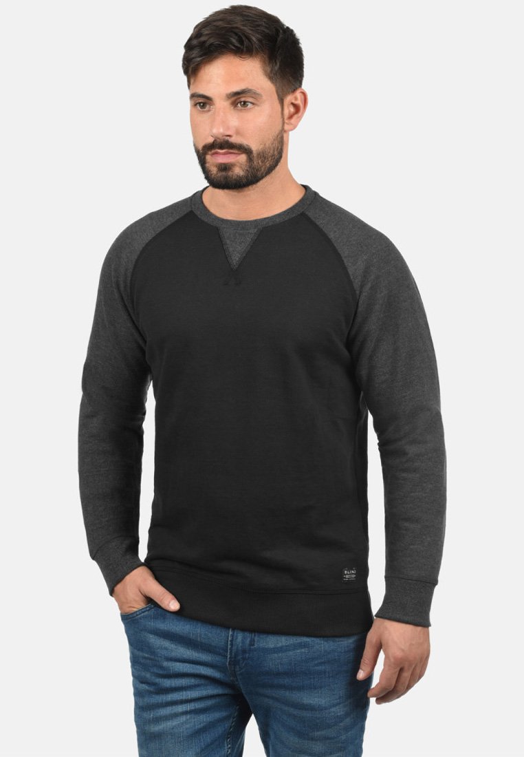Sudadera negra y gris oscuro con mangas raglán, puños y dobladillo acanalados; fabricada en un tejido suave con una textura lisa.