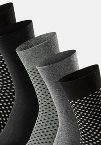 Vijf paren sokken in verschillende tinten zwart en grijs, met effen en stippenpatronen, ribbelboorden en een gladde textuur.