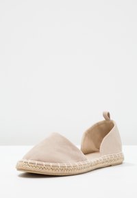 Espadrille plate en daim beige avec bout fermé pointu, talon ouvert, languette de tirage et couture de semelle en jute tressée.
