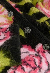 Tissu en tricot duveteux avec des motifs floraux roses et verts, bords côtelés noirs, et boutons noirs avec des motifs de nœuds en argent.