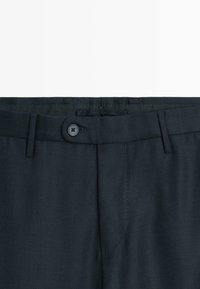 Donker marineblauwe broek van een gestructureerde stof, met een standaard knoopsluiting, riemlussen en scherpe plooien voor een gestructureerde uitstraling.