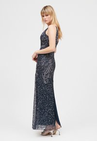 Abito lungo blu navy con decorazioni di paillettes, corsetto aderente e spacco laterale. Abbinato a sandali argentati con cinturini.