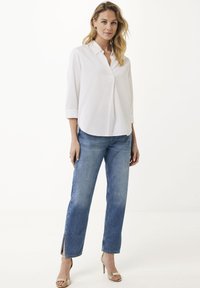 Camicia bianca con colletto, maniche 3/4; abbinata a jeans dritti blu chiaro con fessure laterali. Indossata con tacchi dorati.