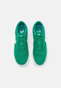 Green canvas sneakers with white accents, flat laces, rounded toe, and a cushioned interior featuring a blue insole.