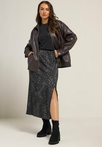 Bruine neplederen jacket over een zwarte top, gecombineerd met een knie-lange donkergrijze luipaardprint rok met een zijsplit en zwarte hoge hakken.