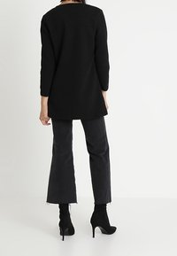 Svart, texturerad långärmad topp, med fållen som täcker höfterna, ihop med svarta utsvängda jeans och svarta klackade ankle boots.