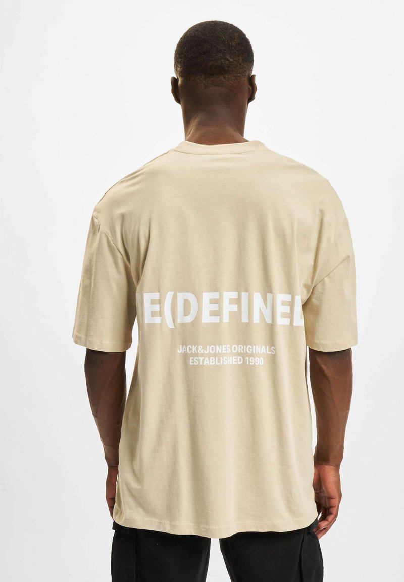 Beige bomull t-skjorte med oversized passform, korte ermer og fet hvit tekst på ryggen, inkludert "E(DEFINED)" og merkevaren logo.