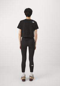 Black cropped t-shirt with short sleeves, paired with black leggings. Both feature the white logo of The North Face. Worn with trail shoes.