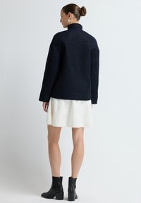 Granatowa teksturowana kurtka z wysokim kołnierzem, zestawiona z białą spódnicą i czarnymi botkami. Posiada luźny krój i długie rękawy.