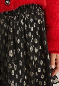 Fekete szoknya fémes arany leopárdmintával, ráncolt derékkal. Pirospozsgás felső részben látható.