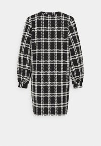 Robe à manches longues à carreaux noir et blanc avec un col rond et des poignets bouffants, vue de dos sur fond blanc.