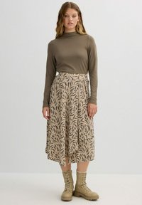 Falda midi de diseño floral en color beige combinada con una blusa de manga larga en tono oliva y botas de cordones color marrón claro; tela suave, diseño fluido y textura sutil.