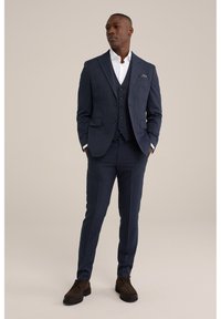 Costume trois pièces à carreaux navy avec une veste à un bouton, des revers en pointe et un pantalon assorti, associé à une chemise blanche impeccable et des chaussures marron.