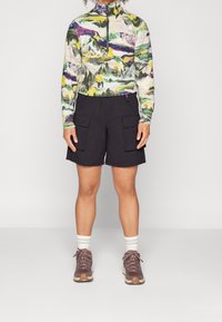 Långärmad, högkragad tröja med ett flerfärgat bergsmönster, tillsammans med svarta cargoshorts och bruna vandringsskor med vita strumpor.