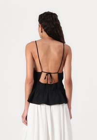 Top noir sans manches avec des fines bretelles, design à dos ouvert, taille cintrée et ourlet évasé. Fabriqué en tissu léger.