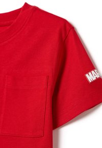 Camiseta de algodón roja con cuello redondo, mangas cortas, un bolsillo en el pecho izquierdo y una etiqueta de logo blanca en la manga. Textura suave.
