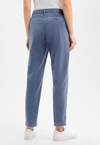 Light blue, loose-fitting cotton trousers with a straight leg, featuring back pockets and a cuffed hem, paired with white sneakers.