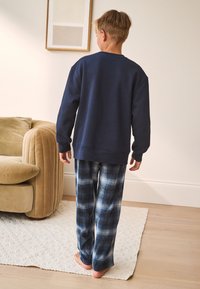Tengerészkék pulóver hosszú ujjakkal és lekerekített nyakkivágással, kék-fehér kockás pizsamanadrággal párosítva, laza szabással.