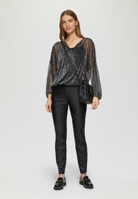 Zwarte, doorschijnende blouse met gestructureerde metallic draden en een losse pasvorm, gecombineerd met zwarte, strakke broek en chunky zwarte schoenen. Kleine crossbody tas.