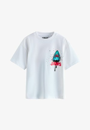 Weißes T-Shirt mit kurzen Ärmeln, bedruckt mit einem blauen Haikopf und rotem "JAWS"-Text auf der Brust, verziert mit schwarzen Farbspritzern.