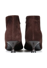 Brązowe zamszowe botki za kostkę z wysmukloną piętą, z zamkiem błyskawicznym i gładką powierzchnią. Obcasy są zakrzywione z czarnym akcentem u podstawy.