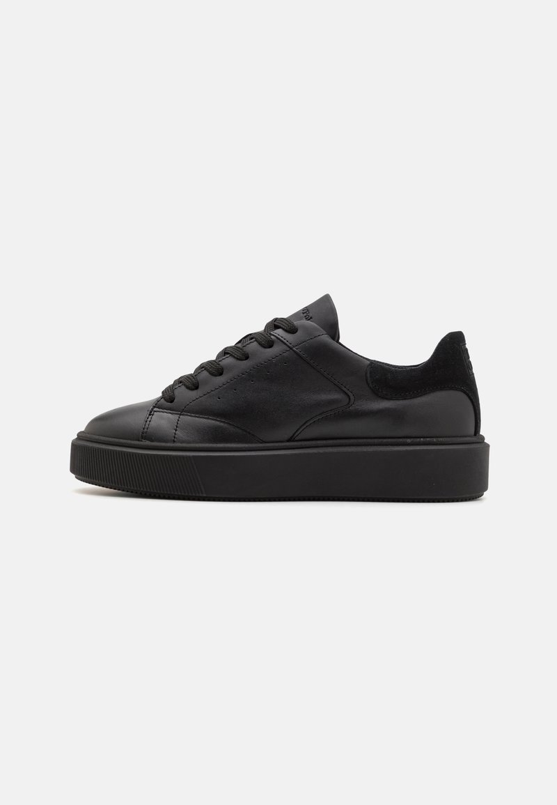 Baskets basses noires avec une semelle épaisse, dessus en cuir et lacets, vues de profil sur un fond clair uni.
