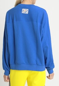 Blå sweatshirt med rund halsringning, löst passform och långa ärmar. Har en fyrkantig logotypapplikation på övre ryggen. Mjuk, texturerad tyg.