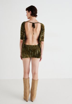 Olivengrønn crop-top med åpen rygg, kort skjørt, teksturert stoff og knyte detaljer i halsen; kombinert med beige støvler til knærne.