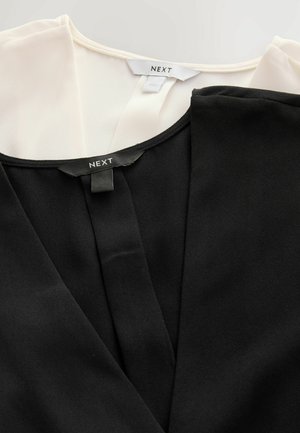 Mustat ja valkoiset paidat roikkuvat vierekkäin, kummassakin on etiketti, jossa lukee "NEXT". Keskity kontrastisiin väreihin ja sileisiin kankaisiin.