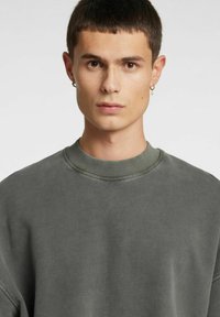 Felpa grigia con collo girocollo a coste e spalle scese. Tessuto morbido con una texture liscia e design minimalista.