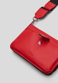 Rød tekstureret læder crossbody taske med klaplukning, metallisk hardware og justerbar rem, med logo prægede på forsiden.