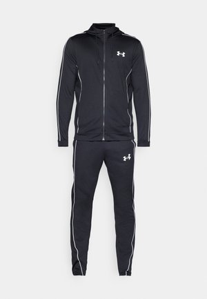 Czarny dres wykonany z gładkiego materiału. Kurtka ma zamek z przodu i kaptur, z białymi paskami po bokach. Spodnie mają dopasowane paski i logo.