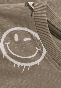 Braunes Baumwoll-T-Shirt mit grauem Smiley-Gesicht; Merkmale einen gerippten Ausschnitt und einen strukturierten Stoff mit einem leicht verwitterten Druckeffekt.