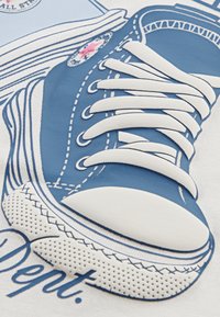 Sinine kangast sneaker'i illustreerimine, millel on valged paelad, kummist tald ja tikandid, ning ringikujuline logo pahkluul.
