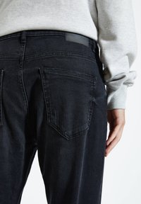 Czarne dżinsy o slim fit, z dwoma tylnymi kieszeniami i skórzaną metką na pasku. Tkanina ma miękką, lekko zużytą fakturę.