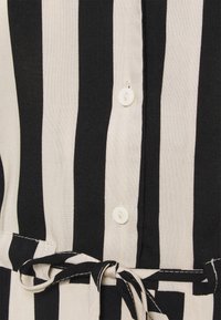 Tessuto a strisce verticali bianco e nero con una finitura texturizzata, dotato di chiusura a bottone e dettaglio in vita annodato per la regolazione.